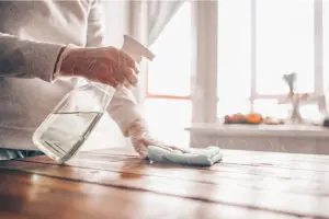Person in a white shirt with gloves wiping down a wooden table with disinfectant to prevent COVID-19