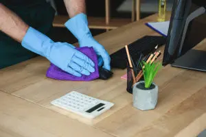 Person with blue gloves sanitizing office technology and electronics on a brown wooden desk