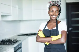 Female maid wearing a white t-shirt, black apron, yellow gloves, and hair wrap while cleaning residential home