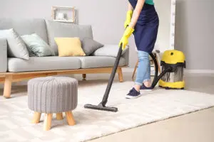 Woman in a blue apron and yellow gloves using a yellow commercial vacuum to clean a residential home in Central Illinois.