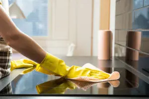 Residential home cleaner wearing yellow gloves and cleaning the surface of an electric stove in Springfield, IL.