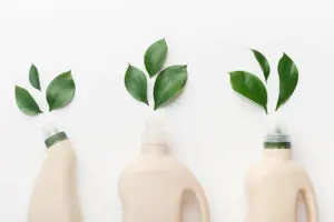 A frontal image of three eco-friendly cleaning products laying on a white table in Springfield, IL with green leaves lying in front of the bottle.