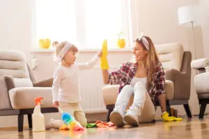 Mother with yellow rubber cleaning gloves and her daughter sitting on the clean floor of their home after residential cleaning service in Springfield, IL.