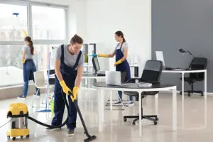 Three commercial janitorial cleaning professionals vacuuming, dusting, and wiping the windows of a business in Springfield, IL.