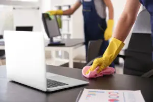 Two commercial cleaning maids wearing yellow gloves are scrubbing the desks and hard surfaces of an office in Springfield, IL in the summer.