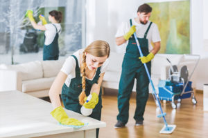 Three cleaning experts wearing yellow gloves and green overalls while cleaning and disinfecting a home