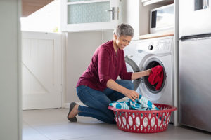 Woman in a red shirt and jeans putting a load of dirty laundry into a modern washing machine