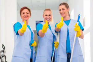 Three women in blue uniforms and yellow gloves giving a thumbs up at their commercial cleaning job