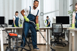 Cleaning company in dark blue uniform and green gloves vacuuming and wiping down commercial office building