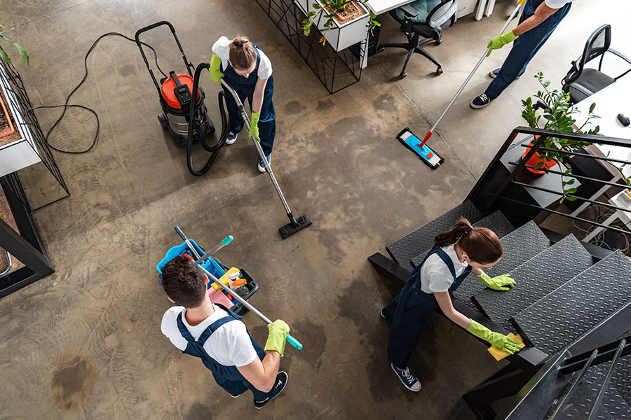 Professional cleaning crew cleaning a commercial office concrete flooring in white t-shirts and blue overalls