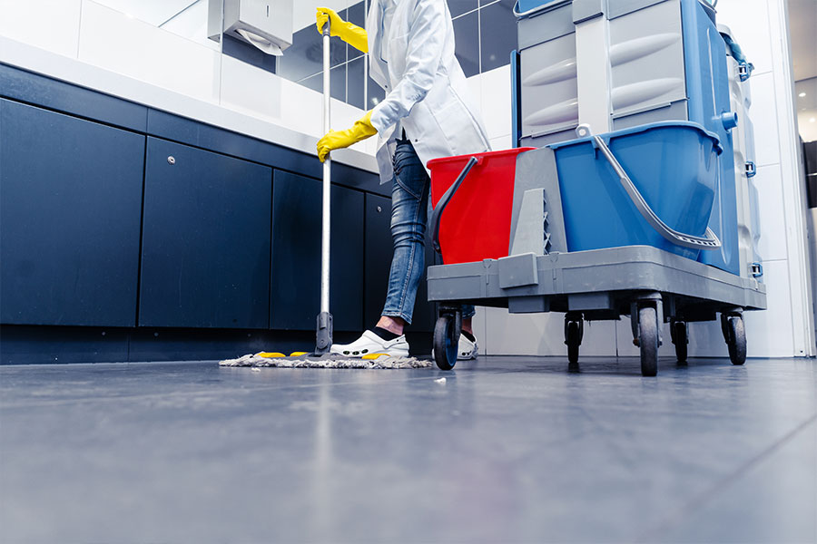 Person in a white cleaning coat and yellow gloves mopping a commercial business’s break room floor