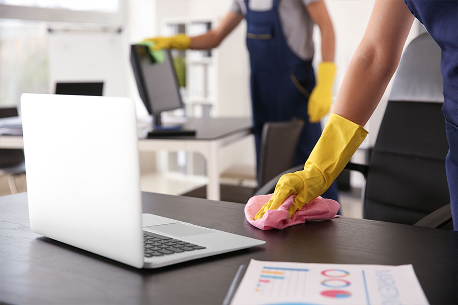 Commercial cleaning crew in dark blue overalls and yellow gloves cleaning and sanitizing office tabletops with a pink washcloth