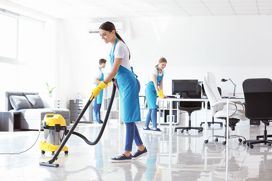 A team of business cleaning professionals in blue aprons and white t-shirts using a yellow commercial vacuum to clean the floor of an office building in Springfield, IL.