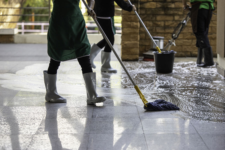 Professional cleaning crew in green aprons and grey rubber boots using commercial cleaning products to mop the floors of a business in Springfield, IL.