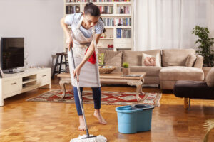 A professional maid in a tan apron using a map and bucket to clean the floors of a living room in Springfield, IL.