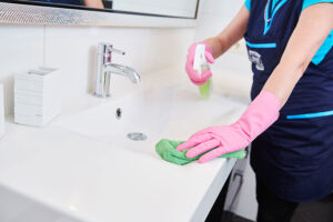 A maid in a blue uniform and pink gloves using a cleaning spray to wipe down a bathroom sink in a residential home in Springfield, IL.