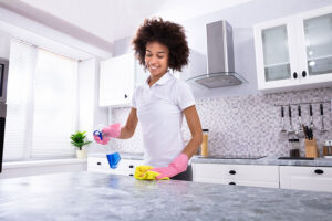 A young maid in a white shirt and pink gloves using a eco-friendly cleaning solution on a kitchen countertop in Springfield, IL.