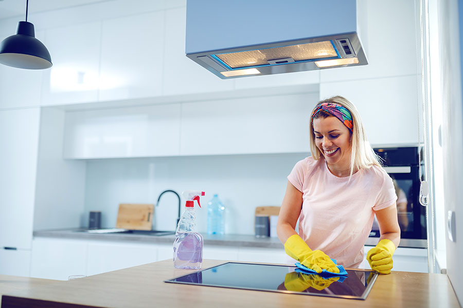 A professional maid in a light pink t-shirt with yellow gloves smiling while cleaning the kitchen of a home in Springfield, IL.