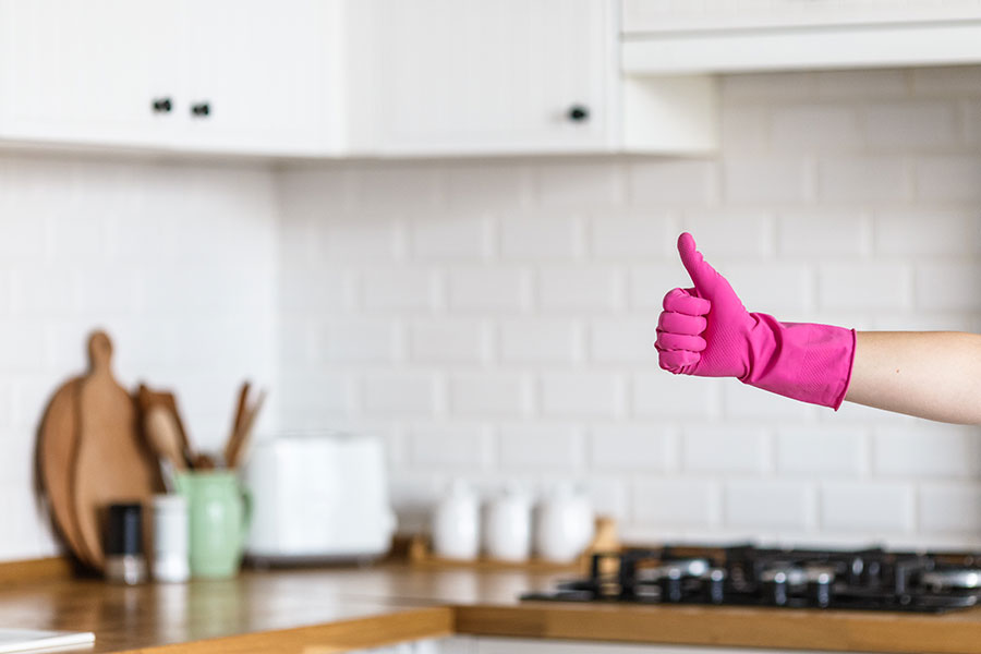 A maid in Springfield, IL, wearing a pink rubber glove holding a thumbs-up sign with a clean residential kitchen in the background.