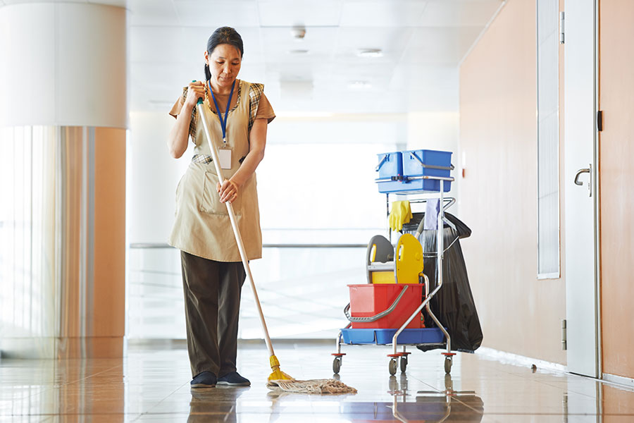 A maid in a tan apron mopping the floor of a commercial business in Springfield, IL with a janitorial cart for cleaning supplies.