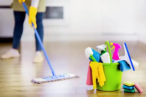 Golden Rule Cleaning & More – A person in Springfield, IL, mopping the floor beside a green bucket filled with cleaning products, sponges, and gloves.