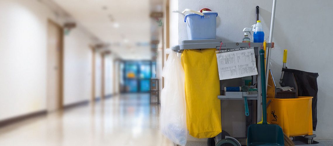Grey cleaning cart with yellow garbage bag placed next to a wall in a commercial business