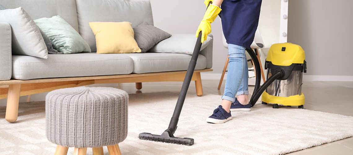 Woman in a blue apron and yellow gloves using a yellow commercial vacuum to clean a residential home in Central Illinois.