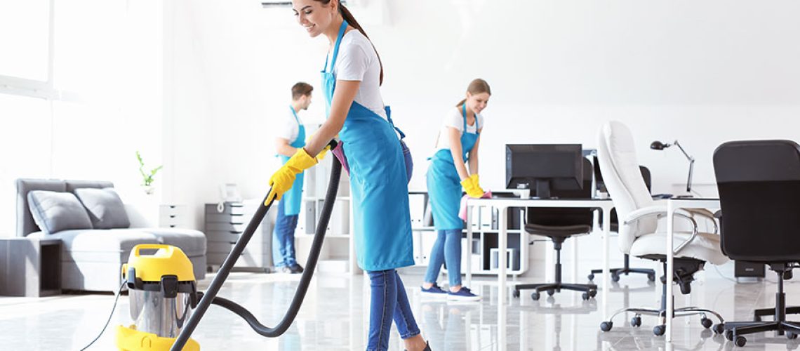 A team of business cleaning professionals in blue aprons and white t-shirts using a yellow commercial vacuum to clean the floor of an office building in Springfield, IL.