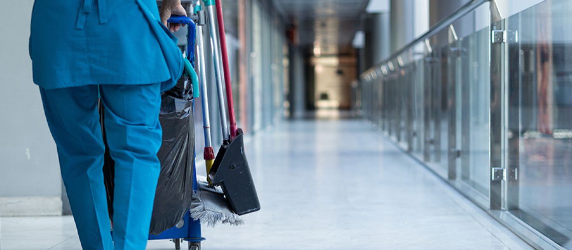 A maid in a blue uniform pushing a janitorial cart down a commercial business hallway in Springfield, IL for a janitorial cleaning service.