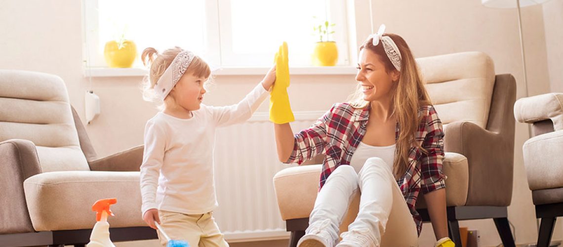 Mother with yellow rubber cleaning gloves and her daughter sitting on the clean floor of their home after residential cleaning service in Springfield, IL.