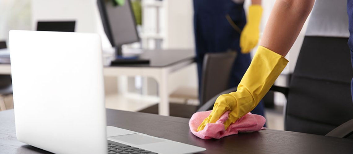 Two commercial cleaning maids wearing yellow gloves are scrubbing the desks and hard surfaces of an office in Springfield, IL in the summer.